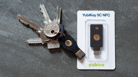 A worn-out USB Type-A security key (a Feitian ePass) laying next to a newer YubiKey USB Type-C model still in its packaging.